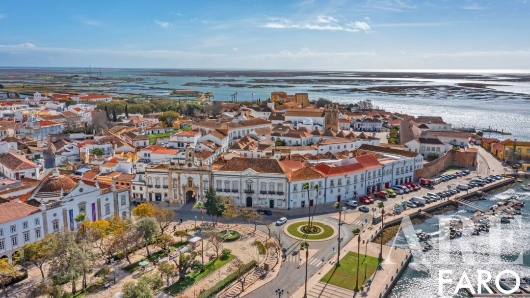 Vista aérea de Faro, con el puerto deportivo en la esquina inferior izquierda, el casco antiguo rodeado de murallas, la Ría Formosa y las islas barrera de Deserta, y Farol en el horizonte